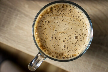 A top view of a frothy coffee mug resting on a wooden surface, showcasing its creamy texture and inviting appearance.