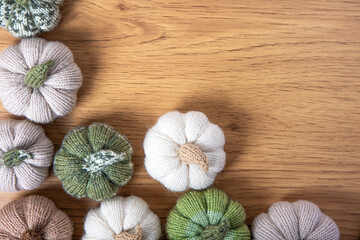 Knitted white, green and beige pumpkins on brown wooden background with place for text. Concept of autumn, Halloween, Thanksgiving. Handmade work. Flat lay, copy space