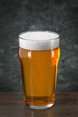 Pint glass with beer on wooden table against the wall in grunge style. Bar theme.  Dark environment. 3d rendering.
