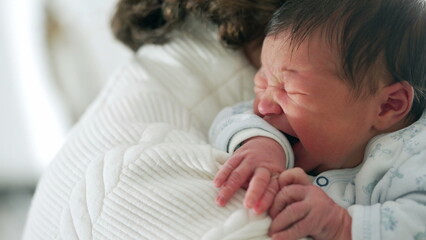 Newborn crying while being held close by grandmother, capturing a moment of distress and comfort,...