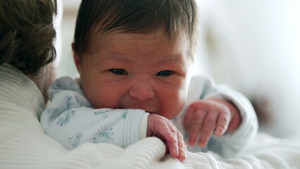 Newborn crying while being held close by grandmother, capturing a moment of distress and comfort,...