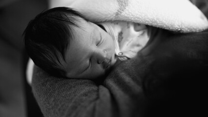 Newborn baby sleeping peacefully in mother’s arms. The intimate scene emphasizes the calm and...