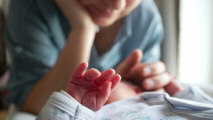 Soft focus on newborn's tiny hand while parent gazes lovingly, illustrating early moments of...