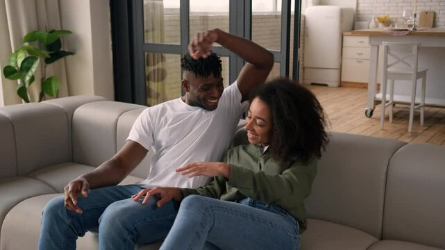 African American happy love couple man woman girl guy fall jump on couch rest casual weekend home relocation moving day own house ethnic family smile homeowner tenant relax cuddle on cozy comfort sofa