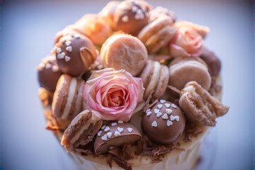 Decorating a scrumptious birthday cake with chocolate, macarons, a pink rose, and chocolate shavings