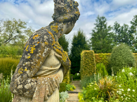 Plou&euml;c-du-Trieux, France, July 24, 2024: Gardens Kerfouler. A close-up view of a weathered statue of Helen of Troy, covered in natural moss and lichen. The statue is set against a lush green backgroun