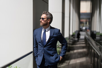 Fototapeta premium Successful ambitious businessman man in businesslike suit standing at modern business office building