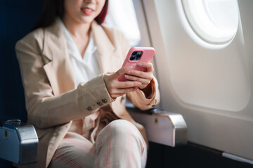 Connected at 30,000 Feet: A young businesswoman effortlessly blends travel and technology, navigating the digital world from the comfort of her airplane seat. 