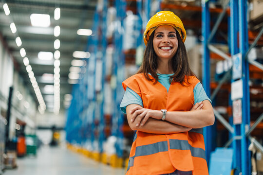 Confident female worker in warehouse arms crossed, smiling bright.