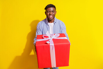 Photo of attractive funny guy wear plaid shirt presenting huge gift emtpy space isolated yellow color background