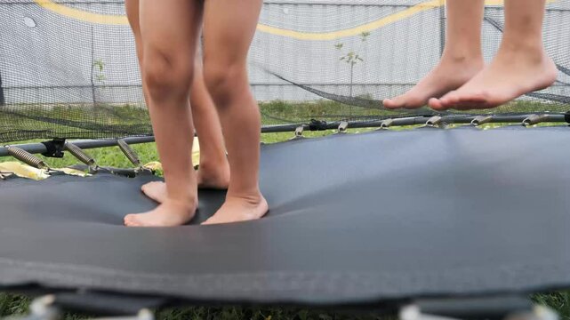 A group of children bounce barefoot on a trampoline in their backyard, enjoying carefree moments and fun under the sun. It's a perfect day for outdoor play.