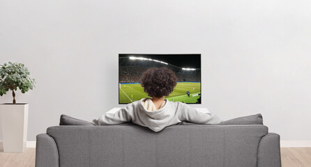 Rear view shot of a guy watching a football match on tv and sitting on a sofa