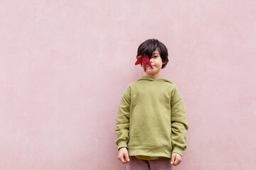 standing child with short dark hair hiding face behind big red leaf