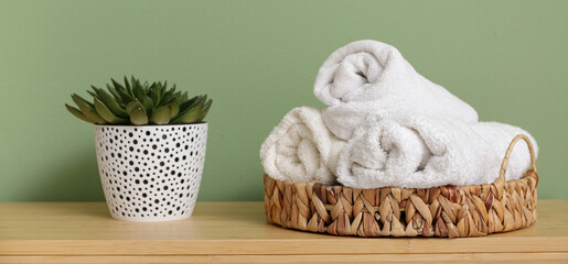 Wicker basket with towels and houseplant on wooden table in bathroom, closeup