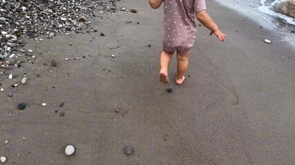 A toddler explores the sandy beach, discovering shells along the shoreline in the afternoon sun - Powered by Adobe