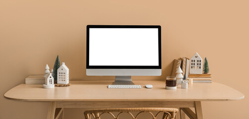 Workplace with computer, candle holders and Christmas trees near beige wall