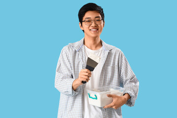 Young Asian man with putty knife and plaster on blue background