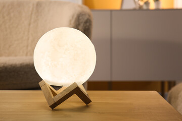 Glowing lamp in shape of moon on wooden table in living room, closeup