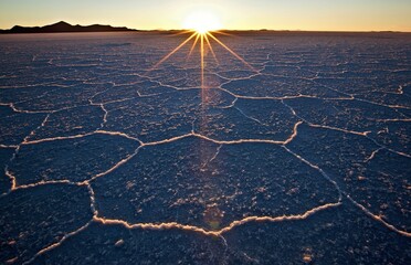 A stunning sunrise over a salt flat, showcasing hexagonal patterns in the landscape.