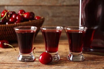 Shots of sweet cherry liqueur and wicker bowl with fresh berries on wooden background