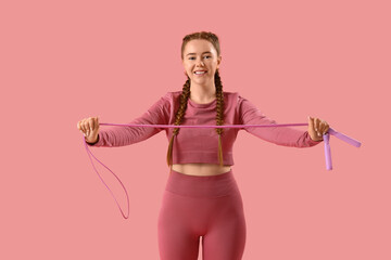 Sporty young woman with skipping rope on pink background