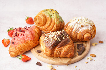 Wooden board with different sweet croissants and strawberries on white background