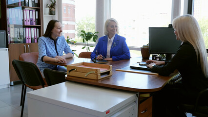Three modern businesswomen sit in corporate office discussing business work negotiations collaboration. Three caucasian females colleagues engage in conversation about work workplace negotiations.