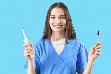 Smiling female dentist with toothbrushes on blue background
