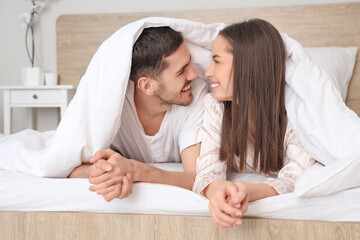 Smiling young couple lying in bed under blanket