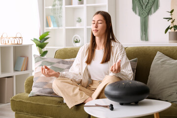 Obraz premium Young woman meditating on sofa with glucophone at home