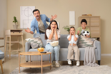 Happy family with snacks and soccer ball watching football game at home