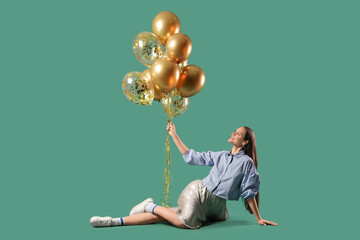 Beautiful young woman with air balloons sitting on green background