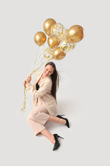 Happy young woman with air balloons sitting on grey background