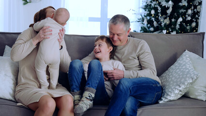 With Christmas tree sparkling in background big family sits on couch,creating cherished memories. Sitting together by Christmas tree large family celebrates their love and togetherness.