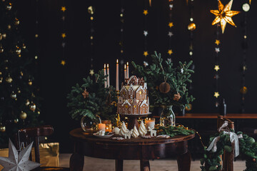 Family holiday celebration. Beautiful traditional homemade gingerbread house. Celebration of Christmas and Happy new year at home. Festive mood, cozy atmosphere, burning candles, fir tree branches