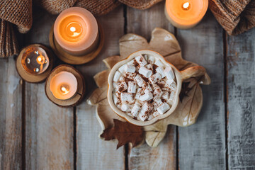 Flat lay top view. Spicy sweet fall hot drink: delicious pumpkin latte with cinnamon, marshmallow. Served in handmade artisan mug in shape of pumpkins, cozy home decor with candles, dry autumn leaves