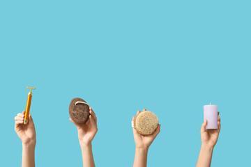 Female hands with massage body brush, facial massage tool, candle and pumice stone on blue background