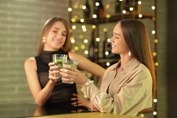 Beautiful young happy women with glasses of mojito in bar
