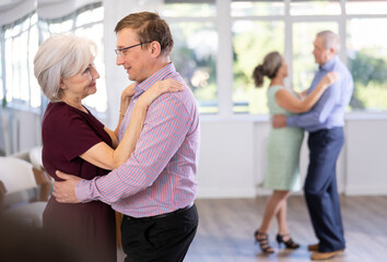 Couple of adult man and elderly woman dancing waltz in studio