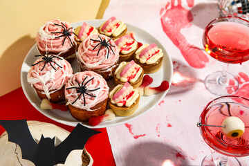 Dessert stand with sweet cakes, glasses of cocktails and decor for Halloween party on color table