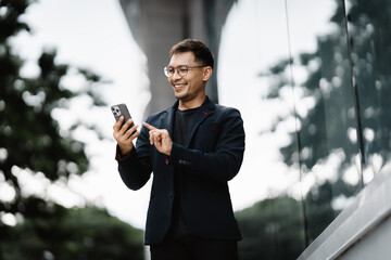 Urban Professional's Digital Delight: A young Asian businessman in a sleek suit enjoys a moment of connection on his smartphone, his smile reflecting the positive news or message he's received. 