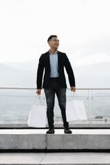 Retail Therapy with a View: Stylish man revels in his shopping spree, bags in hand, against a...