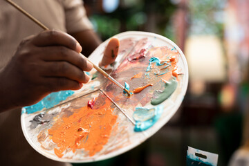 Artist is mixing different dye colors on a palette to create the perfect shade, creating a modern masterpiece on canvas. Male painter using creative tools and supplies for his artwork. Close up.