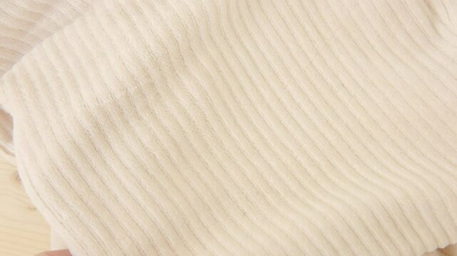 female Hand touching relief texture of beige corduroy cloth or warm fluffy trousers, pants, sewing supplies, checks fabric surface