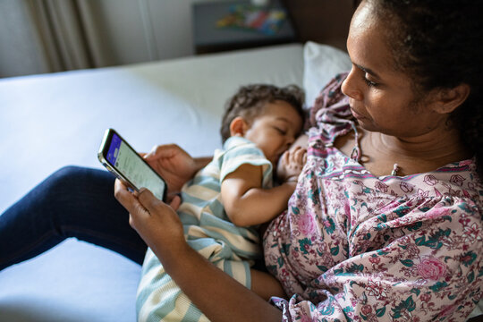 Mother breastfeeding while using smartphone at home
