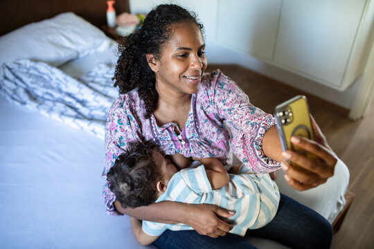 Mother breastfeeding while using smartphone at home