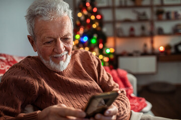 Senior man using smartphone in living room with Christmas tree