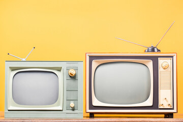 Two retro TVs on table front yellow background. Vintage style filtered photo