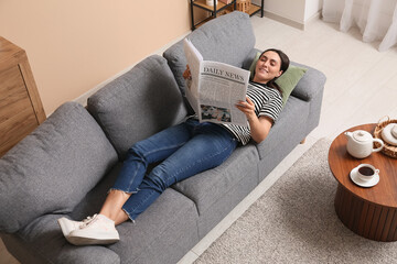 Young woman reading newspaper on sofa at home