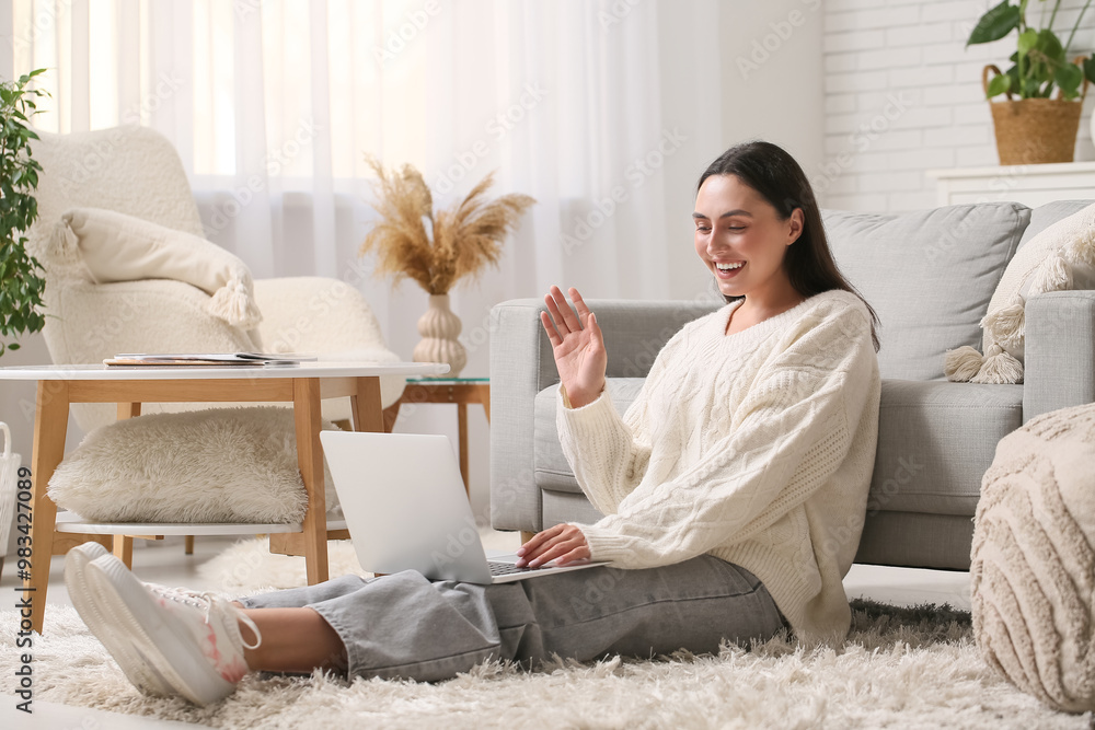 Wall mural Young woman with laptop video chatting on carpet at home